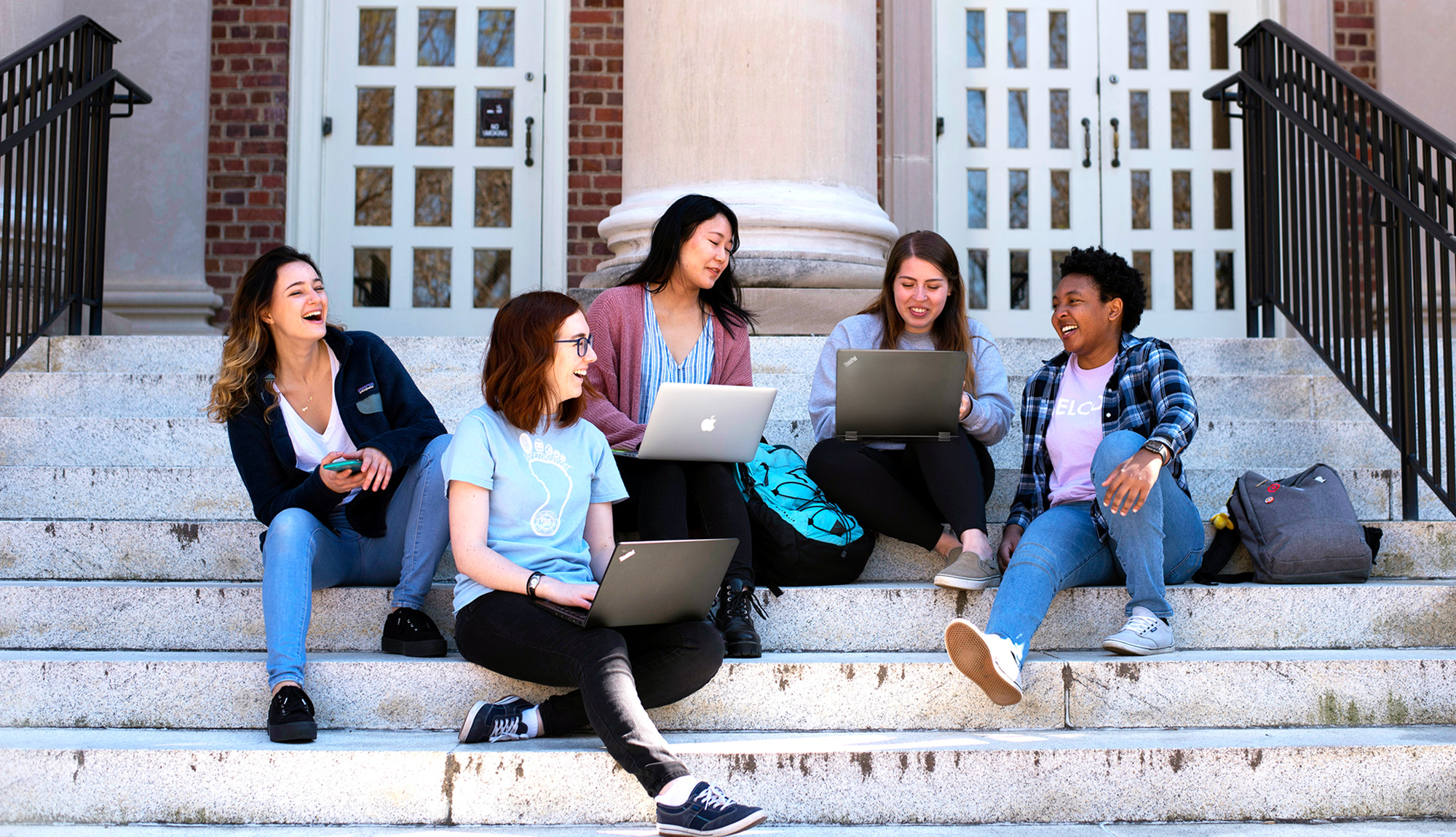 A group of students using laptops on the steps of Wilson Library.